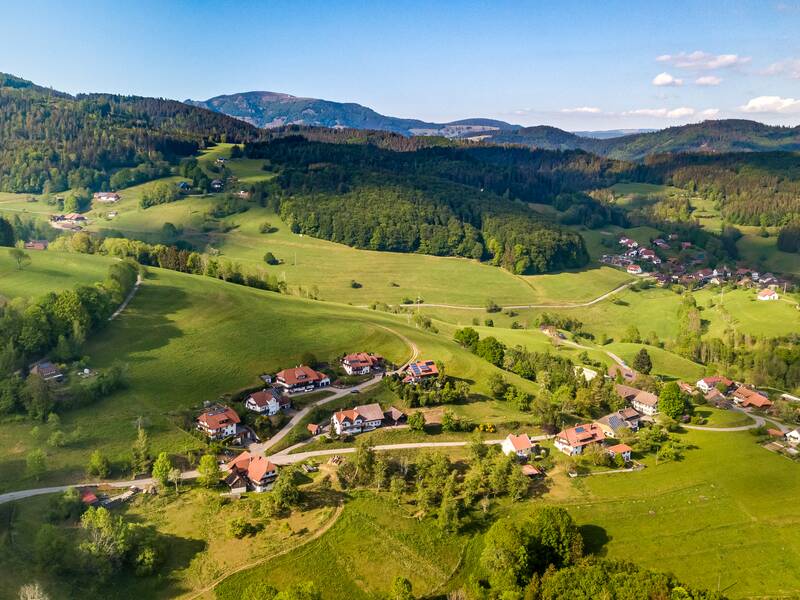 Eine Vielzahl kleiner Dörfer und Gehöfte sind in eine sanft hügelige, grüne Landschaft mit bewaldeten Hügeln im Hintergrund eingebettet.