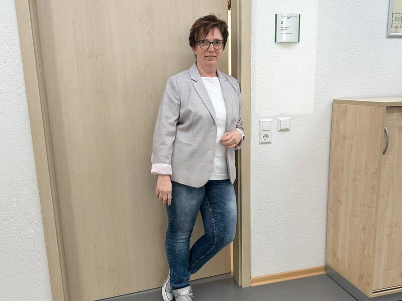 Eine Person steht in legerer Kleidung vor einer Holztür und blickt in die Kamera.